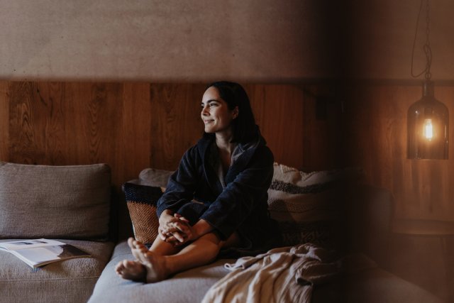 Woman in a bathrobe sitting with a magazine on the sofa by the wooden wall
