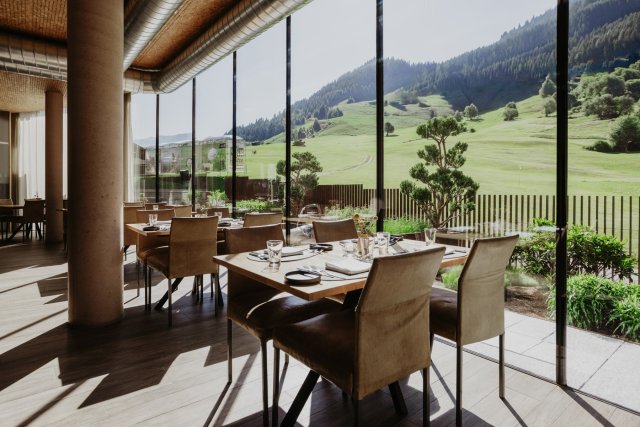Dining room with set tables by the window front, view onto the green golf meadow